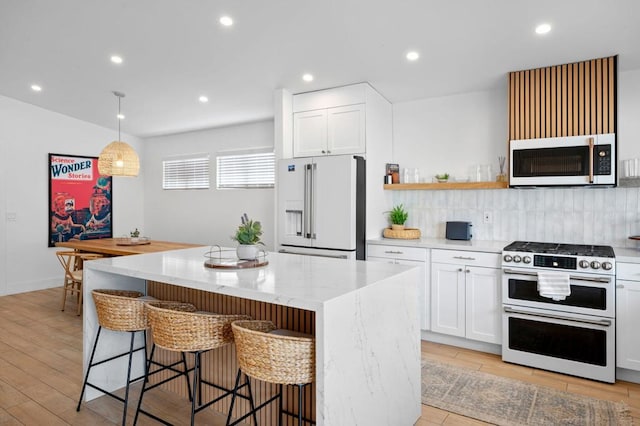 kitchen with decorative light fixtures, white cabinets, high end appliances, and a center island