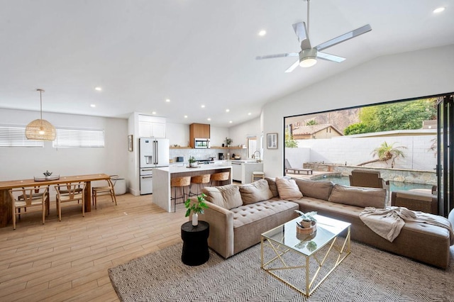 living room with ceiling fan, vaulted ceiling, sink, and light hardwood / wood-style floors