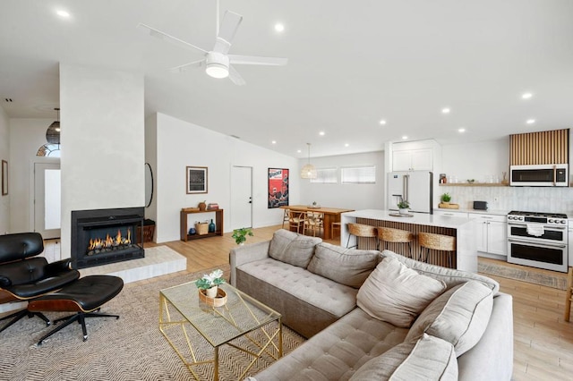 living room with light hardwood / wood-style floors, a large fireplace, ceiling fan, and vaulted ceiling