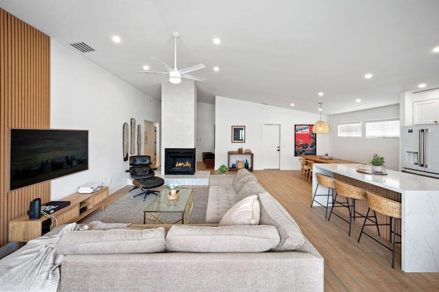 living room featuring ceiling fan, vaulted ceiling, light wood-type flooring, and a fireplace