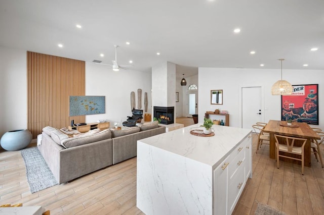 kitchen featuring pendant lighting, white cabinets, a kitchen island, a multi sided fireplace, and ceiling fan