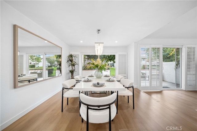 dining room with light wood-type flooring, a healthy amount of sunlight, and a notable chandelier