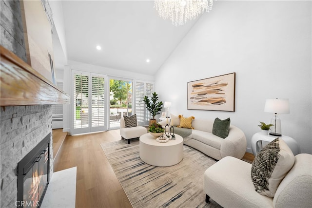 living room featuring a stone fireplace, high vaulted ceiling, a notable chandelier, and light wood-type flooring