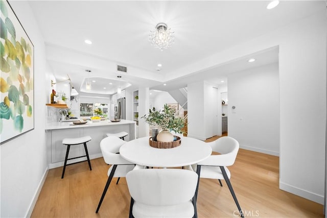 dining area with light hardwood / wood-style floors, a raised ceiling, and a notable chandelier