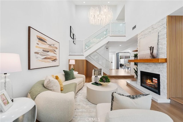 living room with a notable chandelier, a stone fireplace, light wood-type flooring, and a towering ceiling