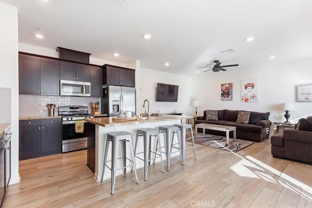 kitchen featuring a center island with sink, a kitchen breakfast bar, light hardwood / wood-style flooring, appliances with stainless steel finishes, and dark brown cabinets