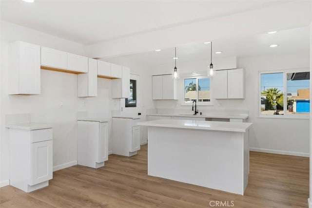 kitchen featuring light wood-type flooring, sink, a center island, white cabinetry, and hanging light fixtures