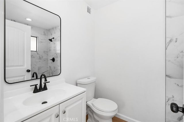 bathroom featuring a tile shower, vanity, and toilet