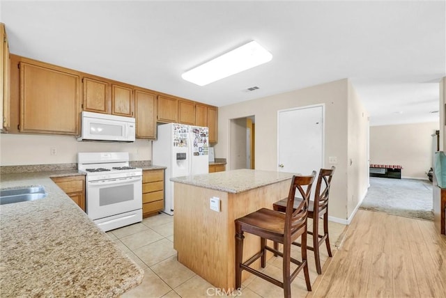 kitchen featuring light stone counters, white appliances, light hardwood / wood-style floors, a kitchen island, and a breakfast bar area