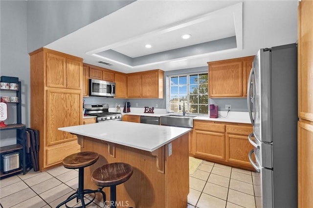 kitchen with appliances with stainless steel finishes, a breakfast bar, a tray ceiling, sink, and a center island