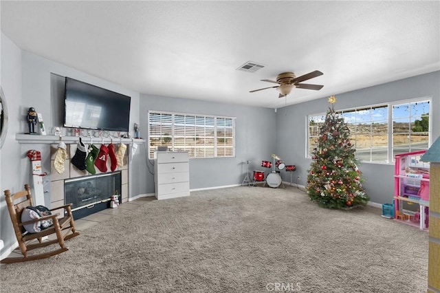 game room with light carpet, a wealth of natural light, a fireplace, and ceiling fan