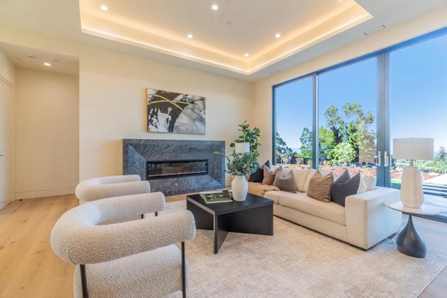 living room with a high end fireplace, light hardwood / wood-style flooring, and a tray ceiling