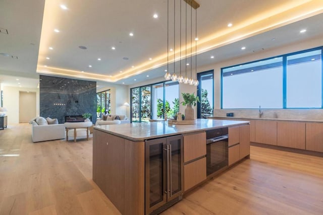 kitchen featuring beverage cooler, decorative light fixtures, black oven, light hardwood / wood-style floors, and a large island