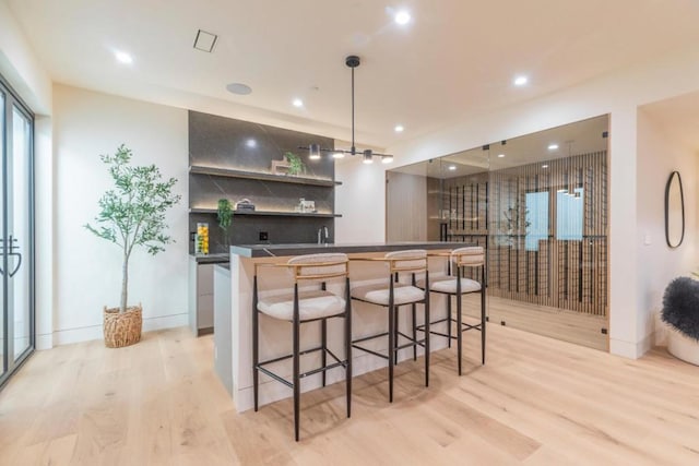 bar with light hardwood / wood-style floors, decorative light fixtures, and backsplash