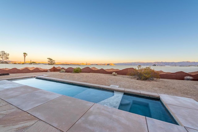 pool at dusk featuring a mountain view and an in ground hot tub