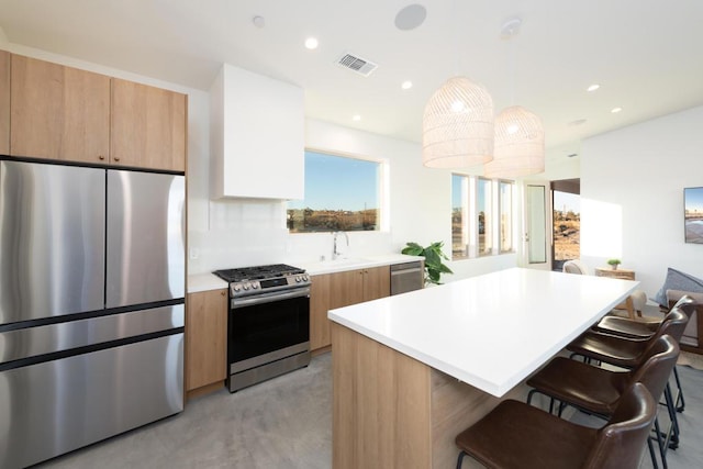 kitchen with appliances with stainless steel finishes, a breakfast bar, sink, a kitchen island, and hanging light fixtures