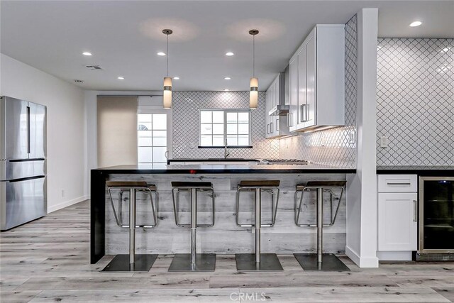 kitchen with a breakfast bar, pendant lighting, white cabinetry, and stainless steel refrigerator