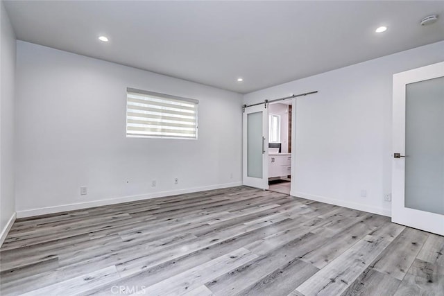 unfurnished bedroom featuring ensuite bathroom, a barn door, and light hardwood / wood-style floors