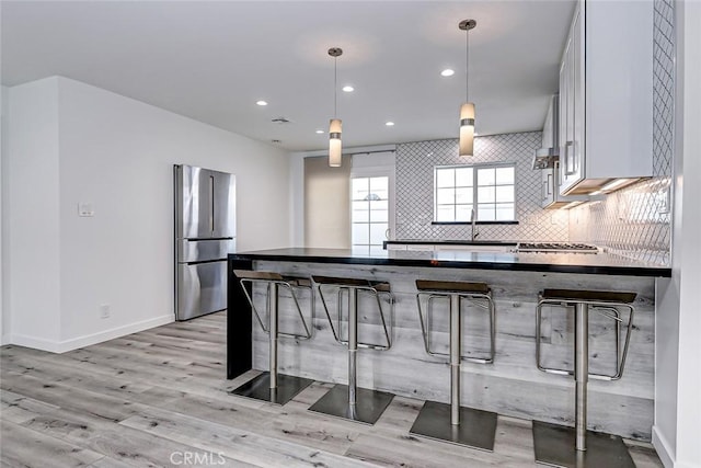 kitchen with pendant lighting, white cabinets, a kitchen breakfast bar, light hardwood / wood-style flooring, and appliances with stainless steel finishes