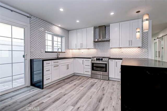 kitchen featuring pendant lighting, wall chimney exhaust hood, stainless steel range, light hardwood / wood-style floors, and white cabinetry