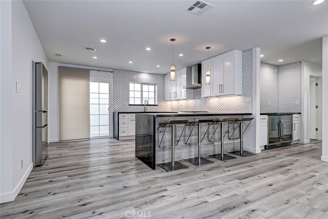 kitchen with light wood-type flooring, beverage cooler, wall chimney range hood, pendant lighting, and white cabinetry