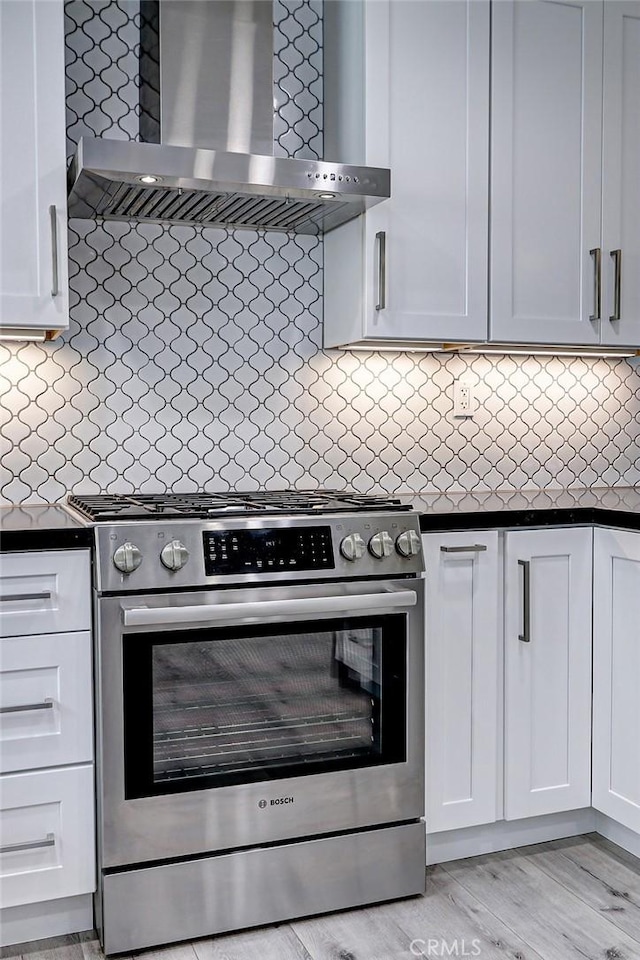 kitchen featuring tasteful backsplash, wall chimney exhaust hood, white cabinetry, and high end range