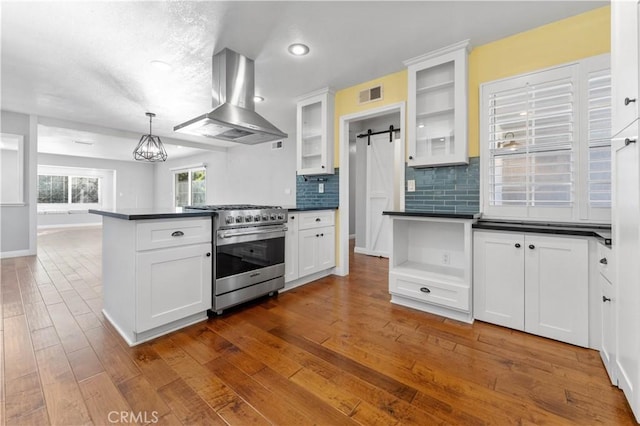 kitchen with dark countertops, high end stainless steel range oven, dark wood-type flooring, white cabinetry, and ventilation hood
