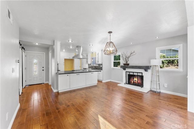 kitchen featuring white cabinetry, wood-type flooring, dark countertops, a wealth of natural light, and wall chimney exhaust hood
