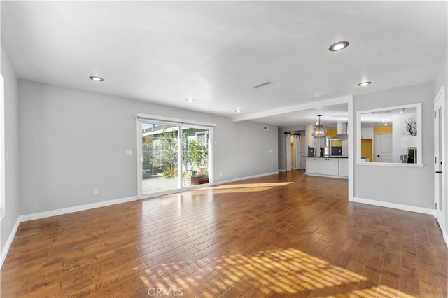 unfurnished living room featuring hardwood / wood-style flooring, a chandelier, baseboards, visible vents, and recessed lighting