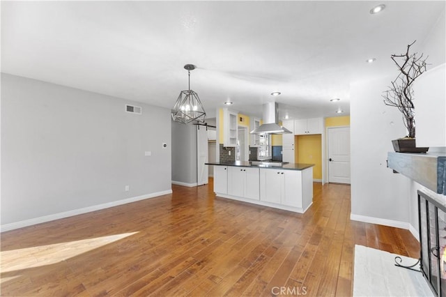 kitchen with white cabinets, visible vents, light wood finished floors, wall chimney exhaust hood, and dark countertops