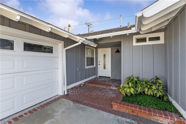 view of exterior entry with driveway, an attached garage, and board and batten siding