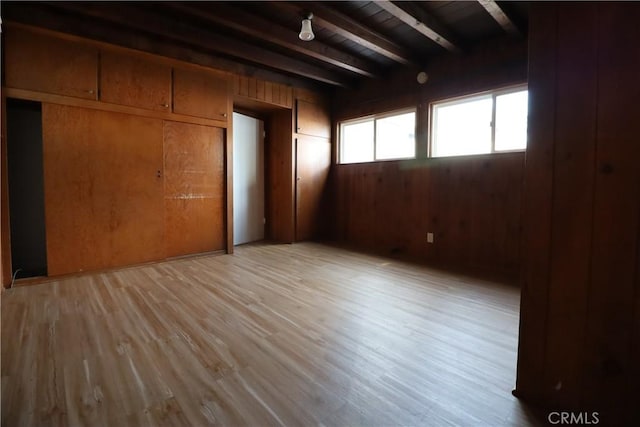 unfurnished bedroom featuring beam ceiling, light wood-type flooring, wooden walls, and wooden ceiling