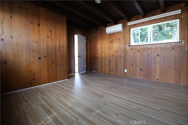 spare room with light wood-type flooring, beam ceiling, wood walls, and an AC wall unit