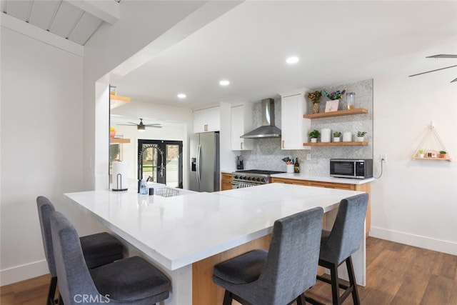 kitchen with a breakfast bar, wall chimney range hood, stainless steel appliances, and kitchen peninsula