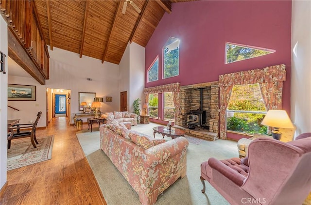 living room featuring beam ceiling, high vaulted ceiling, wooden ceiling, light hardwood / wood-style floors, and a wood stove