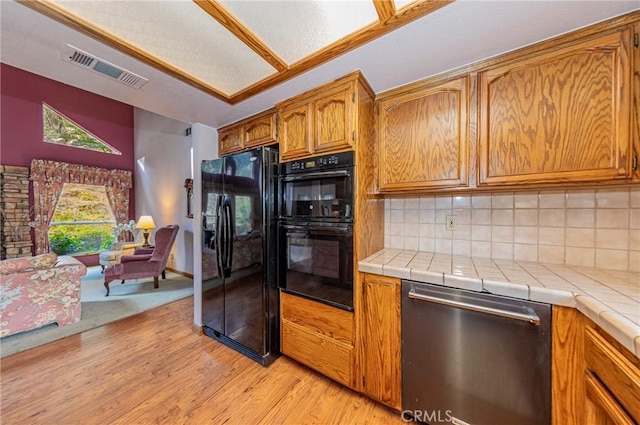 kitchen with decorative backsplash, tile counters, black appliances, and light hardwood / wood-style flooring