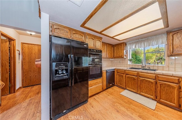 kitchen featuring tile countertops, black appliances, sink, decorative backsplash, and light wood-type flooring