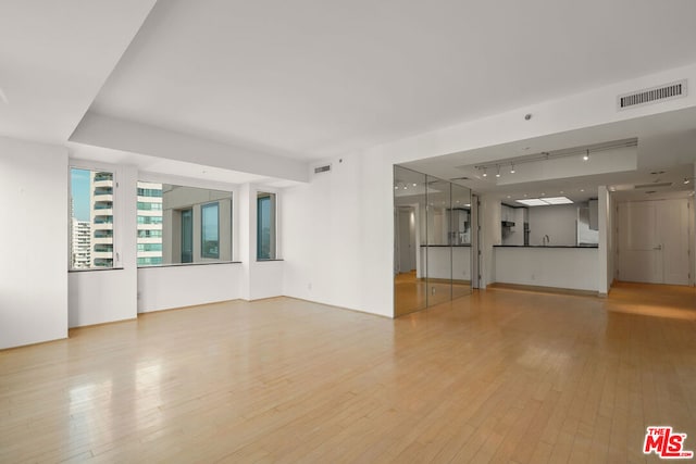 unfurnished living room with light hardwood / wood-style flooring, track lighting, and sink