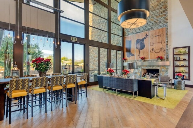 dining space featuring a towering ceiling, wood-type flooring, and a stone fireplace