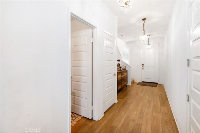 hall with light hardwood / wood-style flooring and an inviting chandelier