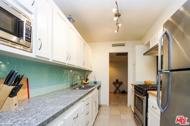 kitchen featuring white cabinets, appliances with stainless steel finishes, light stone countertops, and sink