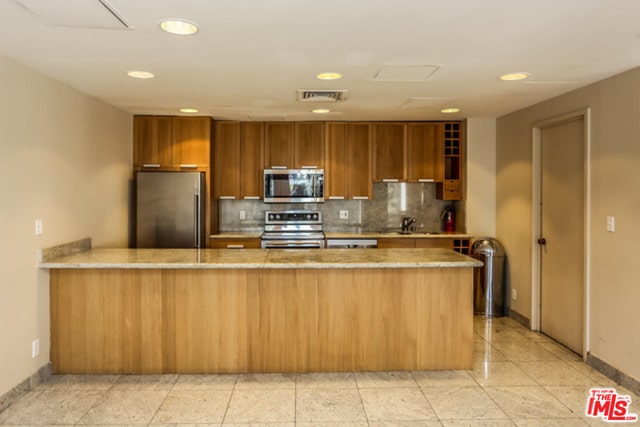 kitchen featuring kitchen peninsula, appliances with stainless steel finishes, tasteful backsplash, light stone counters, and sink