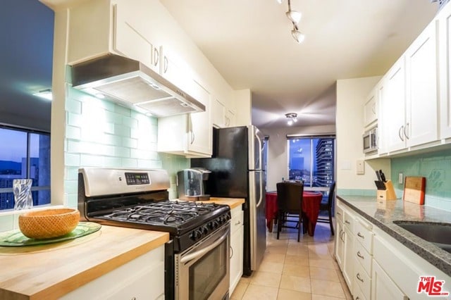 kitchen with white cabinetry, stainless steel appliances, butcher block countertops, decorative backsplash, and light tile patterned floors