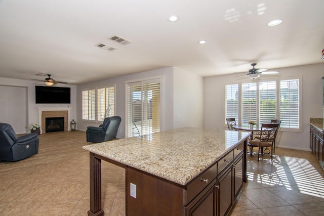 kitchen featuring ceiling fan, light tile patterned floors, light stone counters, and a kitchen island