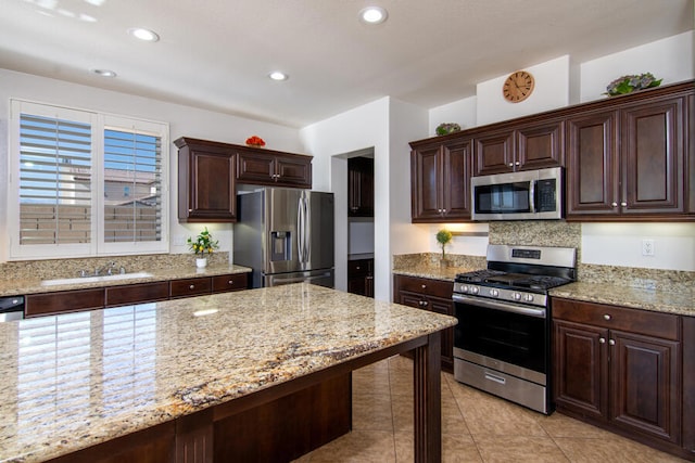 kitchen featuring light stone counters, dark brown cabinetry, sink, and appliances with stainless steel finishes