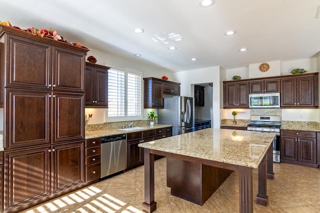 kitchen featuring light stone countertops, a center island, sink, stainless steel appliances, and dark brown cabinets