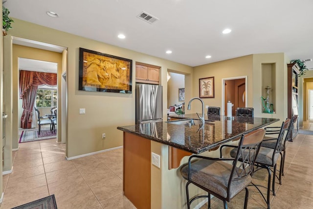 kitchen featuring a breakfast bar, sink, stainless steel fridge, dark stone countertops, and light tile patterned floors