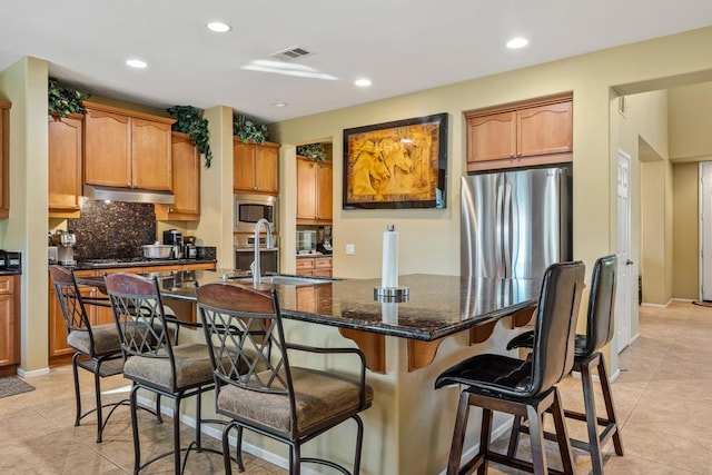 kitchen with sink, dark stone counters, a kitchen island with sink, light tile patterned flooring, and appliances with stainless steel finishes