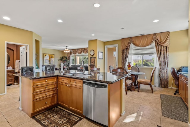 kitchen featuring stainless steel dishwasher, sink, dark stone counters, and an island with sink