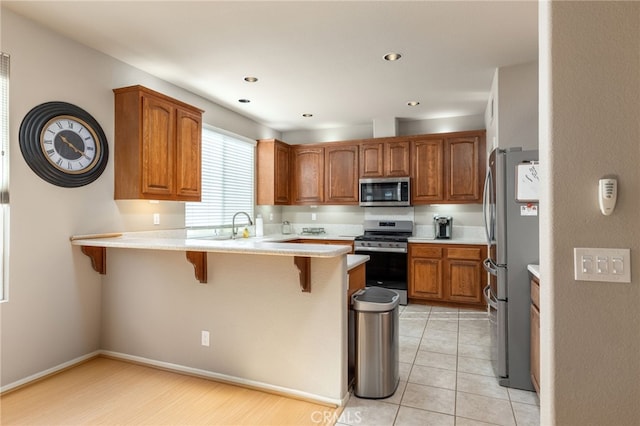 kitchen featuring kitchen peninsula, light tile patterned floors, stainless steel appliances, and a breakfast bar area